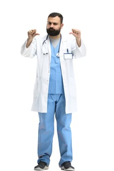 A male doctor, full-length, on a white background, shows his thumbs down.
