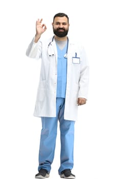 A male doctor, full-length, on a white background, shows an ok sign.