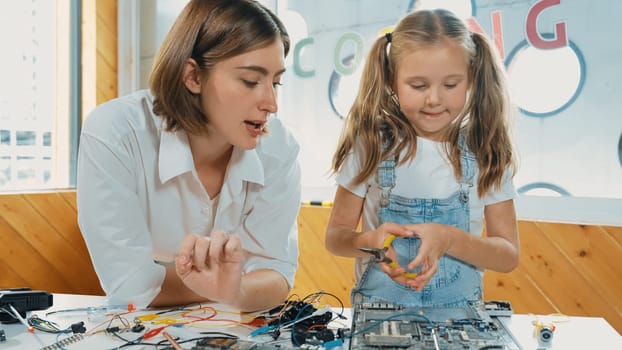 Young smart caucasian teacher teaching students about part of electronic board. Expert girl learn about digital electrical tool and fixing motherboard at table with chips and wires placed. Erudition.