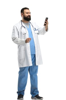 Male doctor, full-length, on a white background, with a phone.