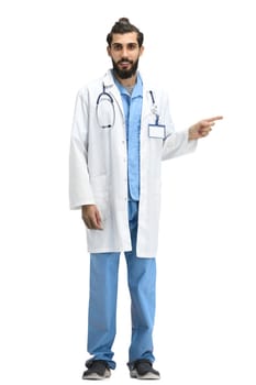 The male doctor, full-length, on a white background, points to the side.