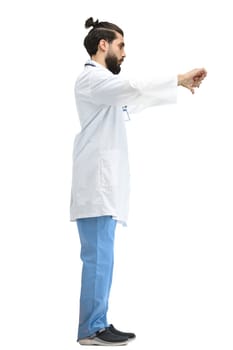 A male doctor, full-length, on a white background, shows his thumbs down.