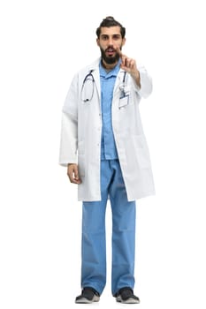 A male doctor, full-length, on a white background, shows a forbidding sign.