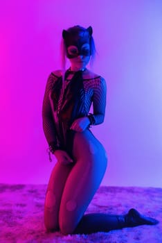 Sexy girl in a latex BDSM mistress dress and a cat mask in neon light on a dark background for sex game