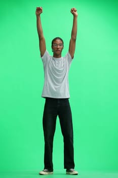 A man in a gray T-shirt, on a green background, in full height, raised his hands.