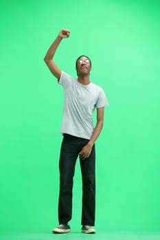 A man in a gray T-shirt, on a green background, in full height, raised his hand up.