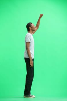A man in a gray T-shirt, on a green background, in full height, raised his hand up.