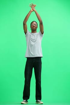 A man in a gray T-shirt, on a green background, in full height, claps.