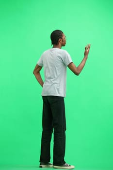 A man in a gray T-shirt, on a green background, full-length, hands on his belt.