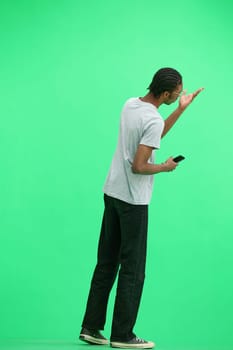 A man in a gray T-shirt, on a green background, full-length, with a phone.