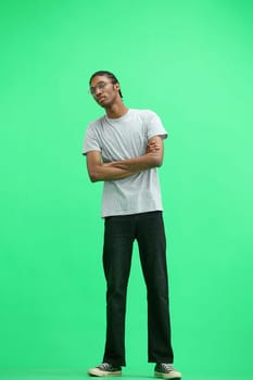 A man in a gray T-shirt, on a green background, in full height, crossed his arms.
