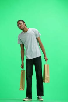 A man in a gray T-shirt, on a green background, full-length, with bags.