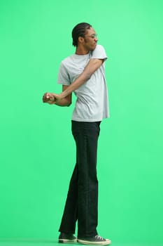 A man in a gray T-shirt, on a green background, in full height, warming up.