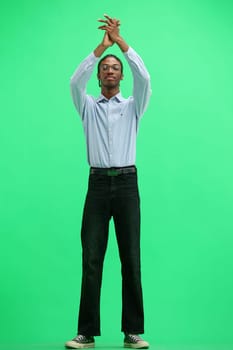 A man in a gray shirt, on a green background, in full height, claps.
