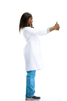 A female doctor, on a white background, in full height, shows her thumbs up.