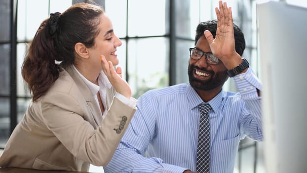 Happy businesswoman using laptop while working with colleague in the office. high five