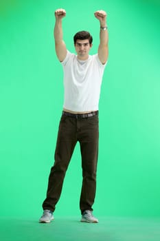A man in full height, on a green background, raised his hands up.