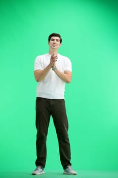A man in full height, on a green background, claps.