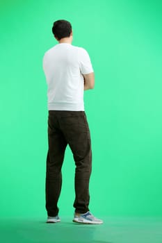 A man, full-length, on a green background, crossed his arms.