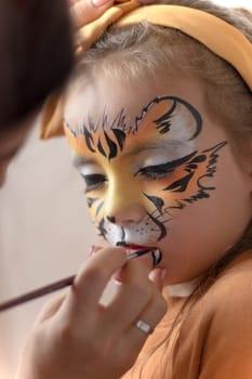 Cute makeup little tiger. face painting outdoors, having fun, copy space. girl with aqua makeup of tiger muzzle. Master making aqua makeup on girl face. aqua grimm on birthday or halloween party