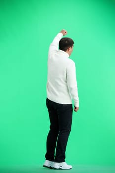 A man, full-length, on a green background, raised his hand up.