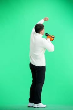 A man, full-length, on a green background, with a megaphone.