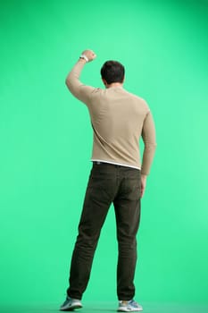 A man, full-length, on a green background, raised his hand up.