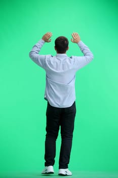 A man, full-length, on a green background, raised his hands up.