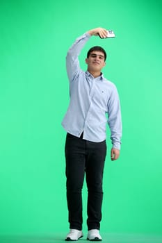 A man, full-length, on a green background, waving his phone.