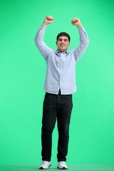 A man, full-length, on a green background, raised his hands up.