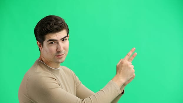 A man, close-up, on a green background, points to the side.