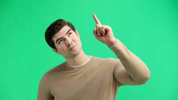 Man, close-up, on a green background, pointing up.