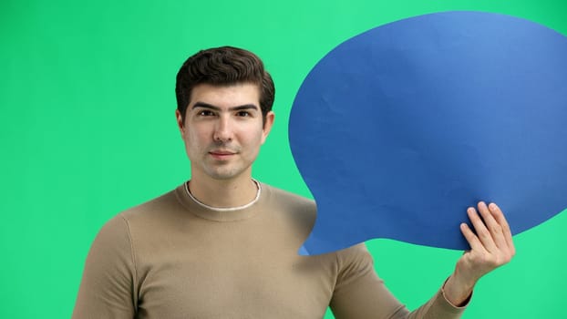 A man, close-up, on a green background, shows a blue comment sign.