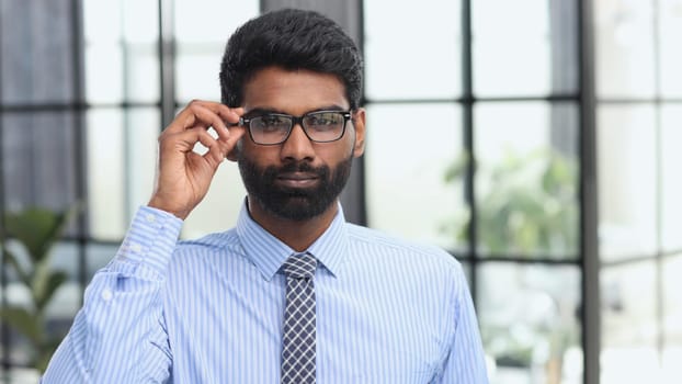 Confident elegant handsome young man standing in the office wearing a blue shirt