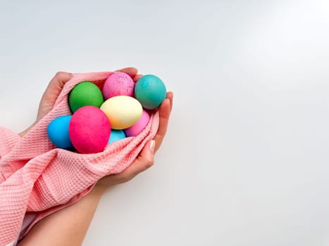 Hands tenderly hold variety of colorful Easter eggs wrapped in soft pink fabric on white background with empty space for text. Suitable for seasonal celebrations and festive spring looks. High quality photo