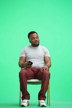 Man, on a green background, sitting on a chair.