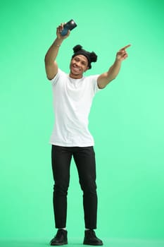 A man, full-length, on a green background, waving his phone.