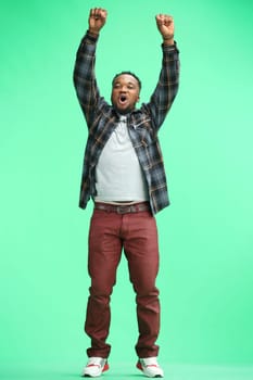 A man, full-length, on a green background, raised his hands up.