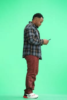 A man, full-length, on a green background, uses a phone.