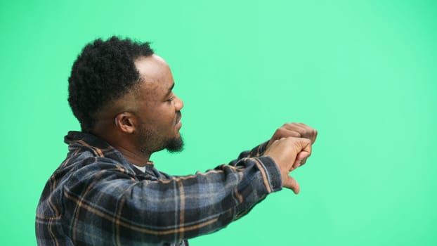 A man, close-up, on a green background, shows his thumbs down.