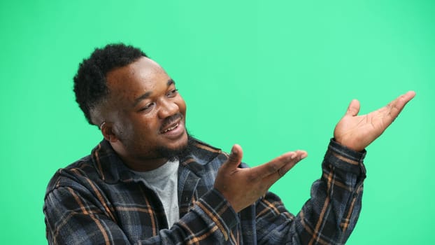 A man, close-up, on a green background, points to the side.