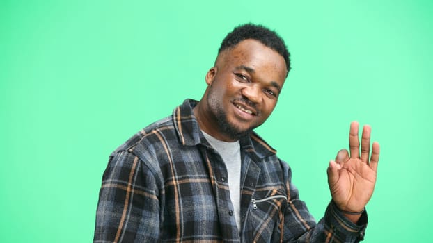 A man, close-up, on a green background, shows an ok sign.