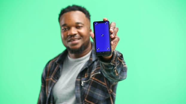 A man, close-up, on a green background, shows a phone.