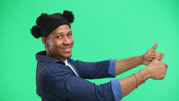 A man, close-up, on a green background, shows his thumbs up.