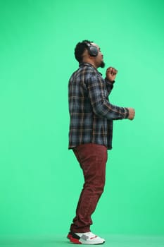 A man, full-length, on a green background, wearing headphones.