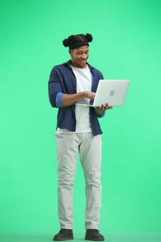 A man, full-length, on a green background, uses a laptop.