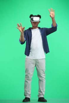 Man, full-length, on a green background, wearing VR glasses.