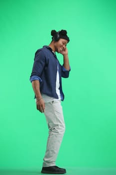 A man, full-length, on a green background, listening to music with headphones.