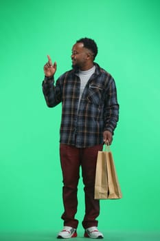 A man, full-length, on a green background, with bags, points up.
