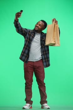 A man, full-length, on a green background, with bags and a phone.